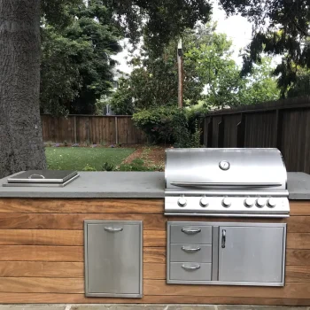 Backyard BBQ island featuring a concrete countertop, built-in stainless steel grill, storage, side burner, and warm wood paneling.