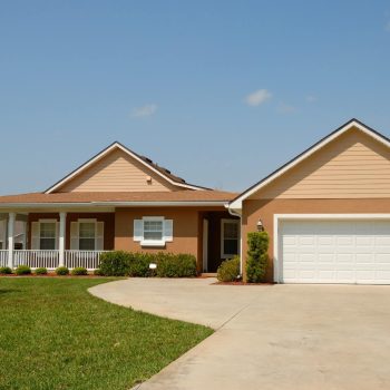 Residential home with a smooth curved concrete driveway leading to a double garage, bordered by manicured lawn and a covered front porch.